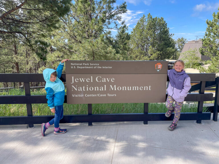 Two girls standing in front of the sign at Jewel Cave National Monument.