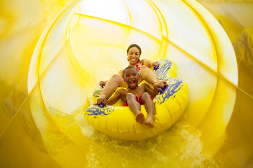 Mother and son sliding down a large yellow tube water slide at Great Wolf Lodge in Scottsdale, Arizona. They have smiles on their faces and are having fun.